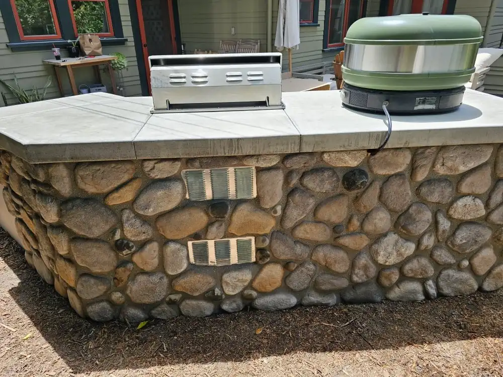 An outdoor kitchen counter faced in river rock with a smooth concrete top